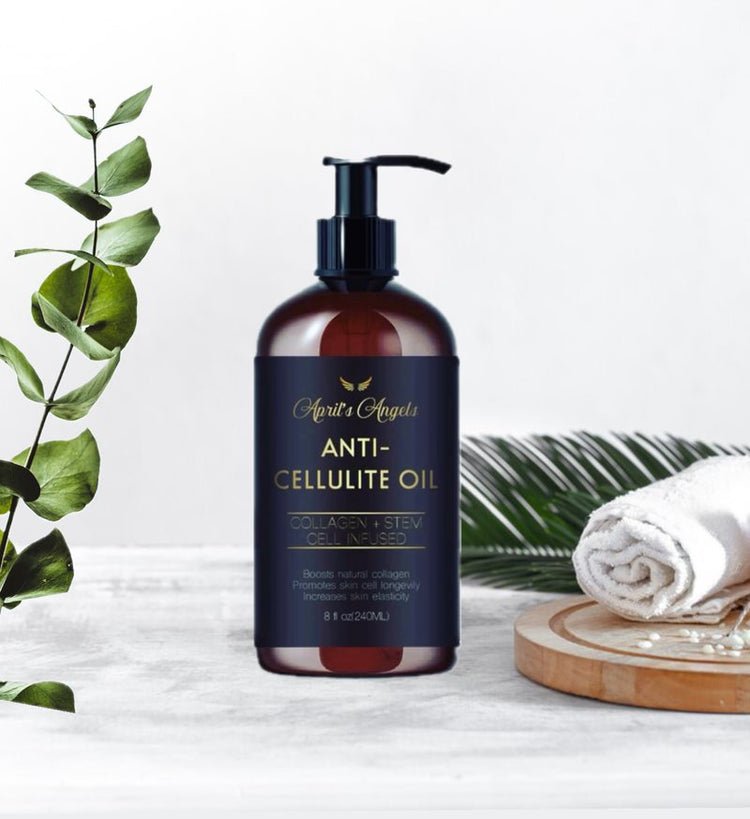 A bottle of Anti-Cellulite Massage oil on a display of skincare with white towel on wood tray, and eucalyptus leaves  